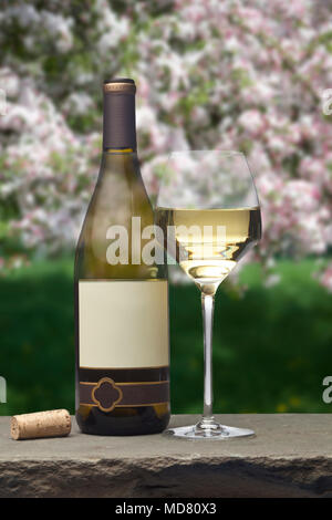 Une bouteille de vin blanc avec une étiquette vierge avec un verre de vin blanc assis sur un comptoir en pierre avec un fond de printemps apple blossoms Banque D'Images