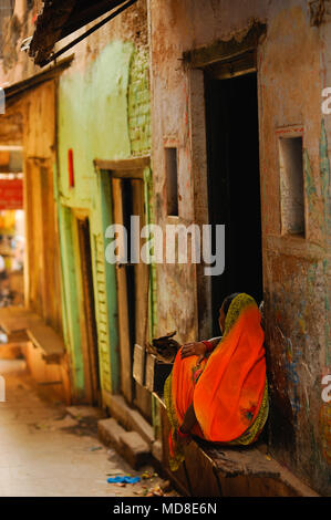 Une dame est assise sur un rebord à l'extérieur de sa maison, dans les petites rues de Varanasi, Inde Banque D'Images
