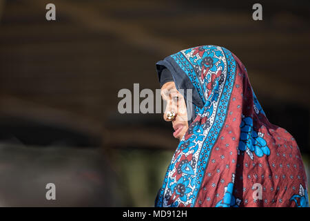 Nizwa, Oman - Mar 23, 2018 : vieille femme omanaise seule dans le soleil avec une expression grave et hijba tout en plissant ses yeux sur une sombre backgroun Banque D'Images