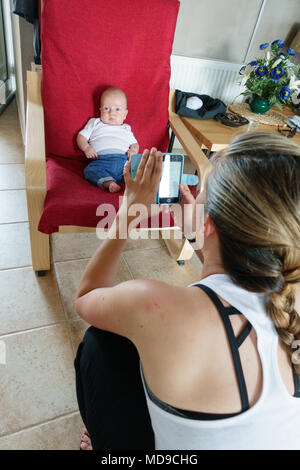 Photographier la mère son bébé garçon assis sur un fauteuil à l'aide de caméra mobile Banque D'Images