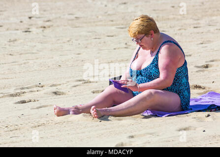 Bournemouth, Dorset, UK. 19 avril 2018. Météo France : belle chaude journée ensoleillée à plages de Bournemouth avec un ciel bleu et soleil ininterrompue, en tant que visiteurs, chef de la mer pour profiter de la journée la plus chaude de l'année jusqu'à présent. Femme assise sur la plage à l'aide de téléphone mobile. Credit : Carolyn Jenkins/Alamy Live News Banque D'Images