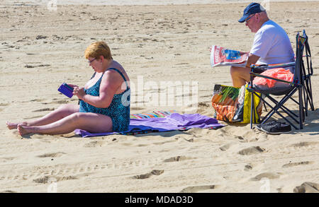 Bournemouth, Dorset, UK. 19 avril 2018. Météo France : belle chaude journée ensoleillée à plages de Bournemouth avec un ciel bleu et soleil ininterrompue, en tant que visiteurs, chef de la mer pour profiter de la journée la plus chaude de l'année jusqu'à présent. D'âge mûr se détendre à la plage, femme textos sur téléphone mobile tandis que l'homme lit les journaux. Credit : Carolyn Jenkins/Alamy Live News Banque D'Images