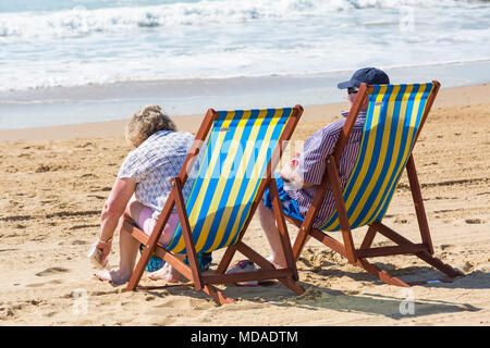 Bournemouth, Dorset, UK. 19 avril 2018. Météo France : belle chaude journée ensoleillée à plages de Bournemouth avec un ciel bleu et soleil ininterrompue, en tant que visiteurs, chef de la mer pour profiter de la journée la plus chaude de l'année jusqu'à présent. Young couple relaxing in transats sur la plage. Credit : Carolyn Jenkins/Alamy Live News Banque D'Images