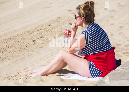 Bournemouth, Dorset, UK. 19 avril 2018. Météo France : belle chaude journée ensoleillée à plages de Bournemouth avec un ciel bleu et soleil ininterrompue, en tant que visiteurs, chef de la mer pour profiter de la journée la plus chaude de l'année jusqu'à présent. Jeune femme assise sur la plage vide bouteille de Coca-Cola. Credit : Carolyn Jenkins/Alamy Live News Banque D'Images