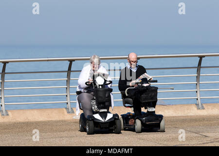 Journée ensoleillée au bord de la mer, Blackpool, Lancashire. 19 avril 2018. Météo britannique. Un couple de personnes âgées s'asseoir dans leur fauteuil motorisé s'asseoir au soleil lire le journal quotidien sur le front de mer de Blackpool, dans le Lancashire. Credit : Cernan Elias/Alamy Live News Banque D'Images