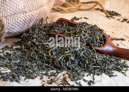 Thé vert chinois. Tas de feuilles de thé sur lin texturé avec cuillère en bambou. Boisson saine et aromatique largement utilisée dans le monde. Banque D'Images