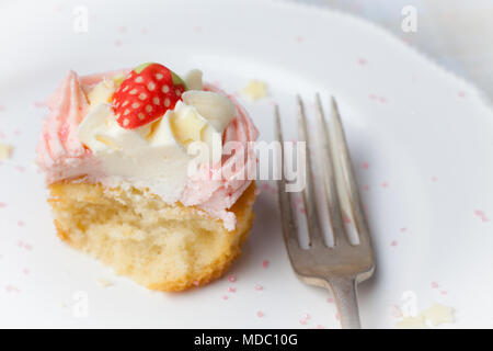 Cupcake fraise rose sur plaque blanche avec étoiles sprinkles, à moitié mangé Banque D'Images