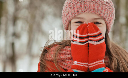 Portrait d'une jeune écolière avec rousseur dans les bois en hiver. Il réchauffe ses mains dans les moufles et les applique sur son visage et des lèvres. Mouvement montre la main dans la main. Banque D'Images