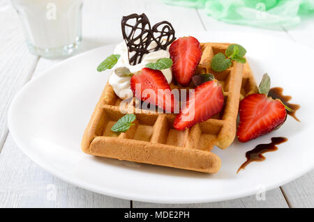 Gaufres de blé entier avec de la crème chantilly, des fraises, les feuilles de menthe et de chocolat sur fond de bois blanc. En bonne santé maison b Banque D'Images