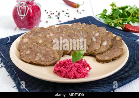 Diététique fait maison de la saucisse de foie sur une table en bois blanc. Couper la saucisse en morceaux dans un plat avec sauce au raifort. Banque D'Images