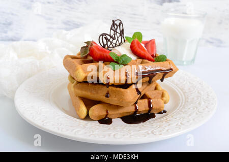 Gaufres de blé entier avec de la crème chantilly, des fraises, les feuilles de menthe et de chocolat sur fond de bois blanc. En bonne santé maison b Banque D'Images