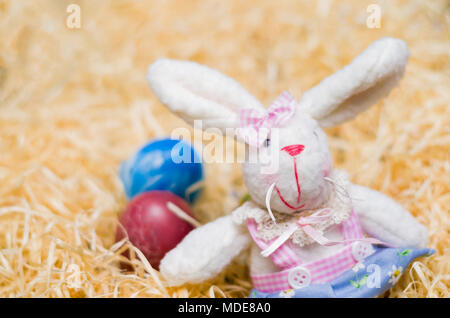 Concept de Pâques, lapin de Pâques en peluche sur fond de paille colorée, décorée avec des oeufs. Banque D'Images