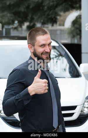 Homme barbu avec l'oreille dans l'oreille près de la voiture montre un geste Banque D'Images