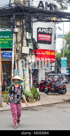 Une Vietnamienne qui traversent la route, et une colonne d'alimentation avec un enchevêtrement de fils électriques et téléphoniques, à Ho Chi Minh City, Vietnam. Banque D'Images