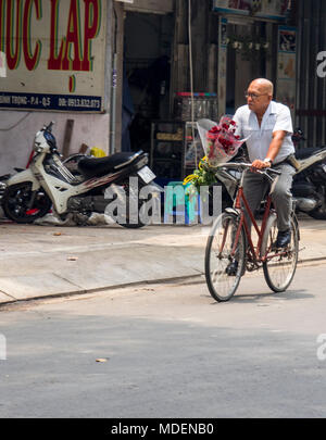 Un vieil homme vietnamien équitation un vélo vintage, portant un bouquet de roses rouges, à Ho Chi Minh City, Vietnam. Banque D'Images