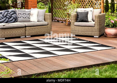 Tapis géométriques noir et blanc sur la terrasse en bois avec des meubles en rotin Banque D'Images