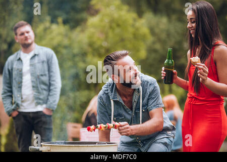 Smiling couple having a barbecue avec leurs amis dans le jardin Banque D'Images