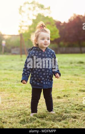 Little baby girl joue heureux dans le parc à l'extérieur dans le ressort contre le rétro-éclairage. Banque D'Images