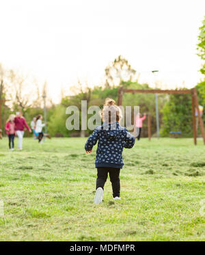 Petite fille s'étend de derrière dans le parc à jouer avec d'autres enfants.
