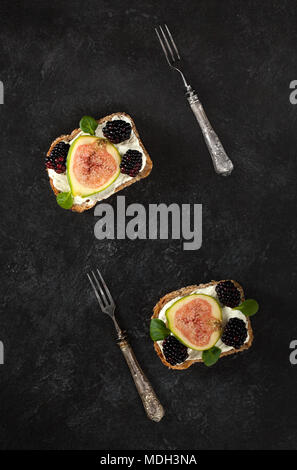 Têtes de pain complet avec du fromage crémeux toasts, figues, mûres et songino feuilles. Vue d'en haut. Banque D'Images