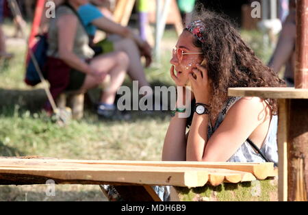 Femme en serre-tête floral, assis et talking on mobile phone au festival de Glastonbury, Somerset, UK 2017 Banque D'Images