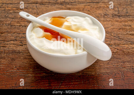 Bio en direct du yaourt grec avec du miel dans un bol en céramique blanche contre grunge, weatheredm bois Banque D'Images