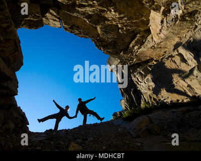Un jeune couple de l'escalade dans la bouche d'une caverne, se tenant la main et en cours de jeu ; Fernie (Colombie-Britannique), Canada Banque D'Images