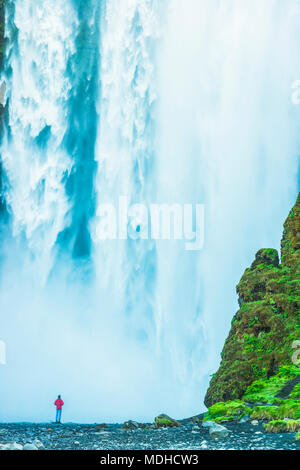 Homme debout à la base de la cascade de Skogafoss ; l'Islande Banque D'Images