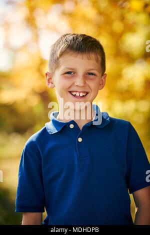 Portrait d'un jeune garçon avec un sourire à pleines dents et à l'automne feuillage coloré à l'arrière-plan ; Ontario, Canada Banque D'Images