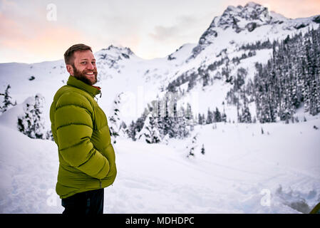 Portrait d'un homme debout, dans les montagnes enneigées au crépuscule ; British Columbia, Canada Banque D'Images