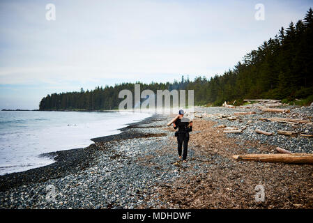 Une femme marche le long d'une plage rocheuse à la collecte du bois dans le parc provincial de Cape Scott, l'île de Vancouver, Colombie-Britannique, Canada Banque D'Images