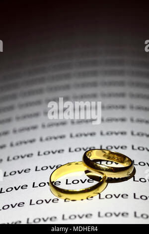 Deux anneaux de mariage d'or sur une page avec le mot amour répété Banque D'Images