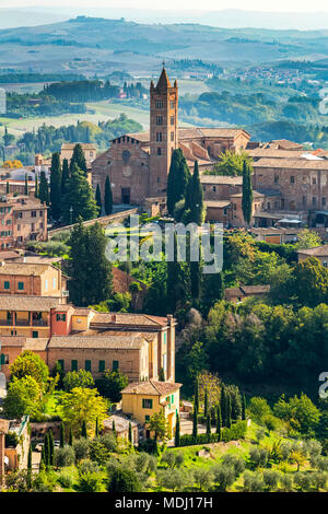 Les bâtiments en pierre et l'église sur le paysage couvert d'arbres et collines en arrière-plan ; Sienne, Toscane, Italie Banque D'Images