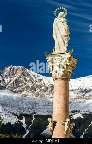 Statue de pierre avec halo en haut de colonne à l'aide d'une chaîne de montagnes couvertes de neige et ciel bleu en arrière-plan, Innsbruck, Tyrol, Autriche Banque D'Images