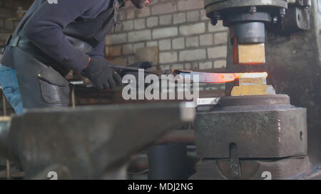 Homme forgeron forge le métal au marteau mécanique Banque D'Images