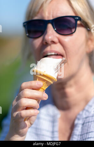 Woman wearing sunglasses holding et lécher une glace à la vanille dans un cône.avec un chocolat en flocons. Soft focus sur son visage. Banque D'Images