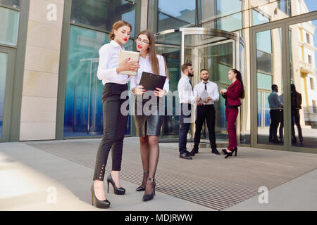 Femme d'affaires. Le personnel de bureau. Deux jeunes filles avec des tablettes électroniques communiquer contre l'arrière-plan d'un verre à plusieurs étages et un immeuble de bureaux Banque D'Images