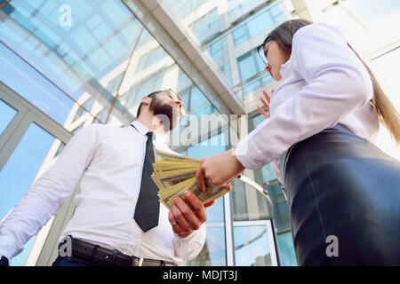 Une jeune fille donne à un homme dans les mains de l'argent dans l'arrière-plan d'un immeuble de bureaux. Le paiement des services. Salaire dans l'enveloppe. Pot-de-vin. la corruption. Sha Banque D'Images