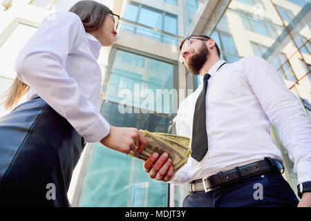 Une jeune fille donne à un homme dans les mains de l'argent dans l'arrière-plan d'un immeuble de bureaux. Le paiement des services. Salaire dans l'enveloppe. Pot-de-vin. la corruption. Sha Banque D'Images