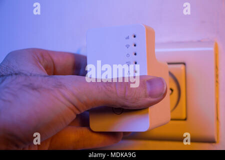 Insérer l'homme dans le répéteur WiFi prise électrique sur le mur. L'aide de l'appareil d'étendre un réseau sans fil à la maison ou au bureau. Banque D'Images
