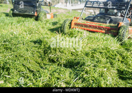 Tas d'herbe verte nouvelle-fauchées avec deux tondeuses derrière. Se concentrer sur l'herbe Banque D'Images