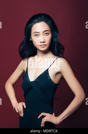 Confiant belle asiatique fille en robe noire, les mains sur les hanches. Joli portrait mannequin Banque D'Images