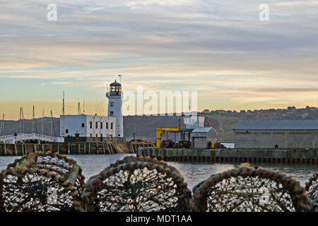 Des casiers à homard et le phare. Le phare de Scarborough et l'entrée du port à la tombée de la nuit, éclairé par la lumière du soleil couchant. Banque D'Images