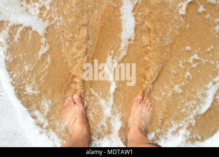 Vue de dessus de la jambe d'un homme debout sur le sable et recouverts par l'o Banque D'Images