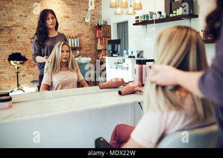 Jeune femme blonde assise sur une chaise à parler avec son coiffeur tout en ayant ses cheveux au cours d'un rendez-vous salon Banque D'Images