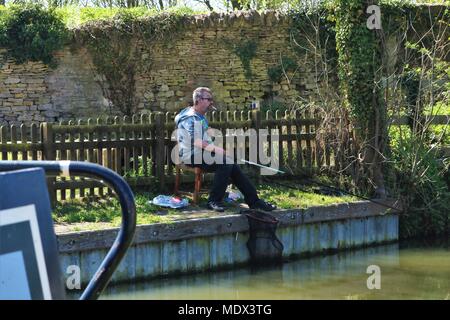 White middle aged man with cigarette en bouche à la pêche du côté de canal au soleil à quai, Enslow Oddington, Oxfordshire Banque D'Images