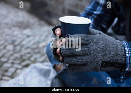 La main de mendiant portant des gants Holding Disposable Cup Banque D'Images