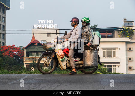 Couple riding a motorcycle chargés de conteneurs dans le vieux quartier de Hanoi, Vietnam ; Banque D'Images