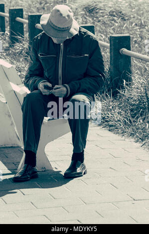 Un homme assis sur un banc en bois, regarde sur son téléphone mobile Banque D'Images