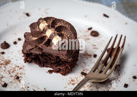 Cupcake chocolat sur plaque blanche avec fourche, saupoudrées de poudre de cacao et de vermicelles de chocolat, à moitié mangé Banque D'Images